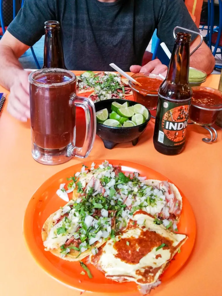 Two plates full of tacos and a beer and a michelada on a table at taqueria alvaro obregon at roma norte, mexico city.