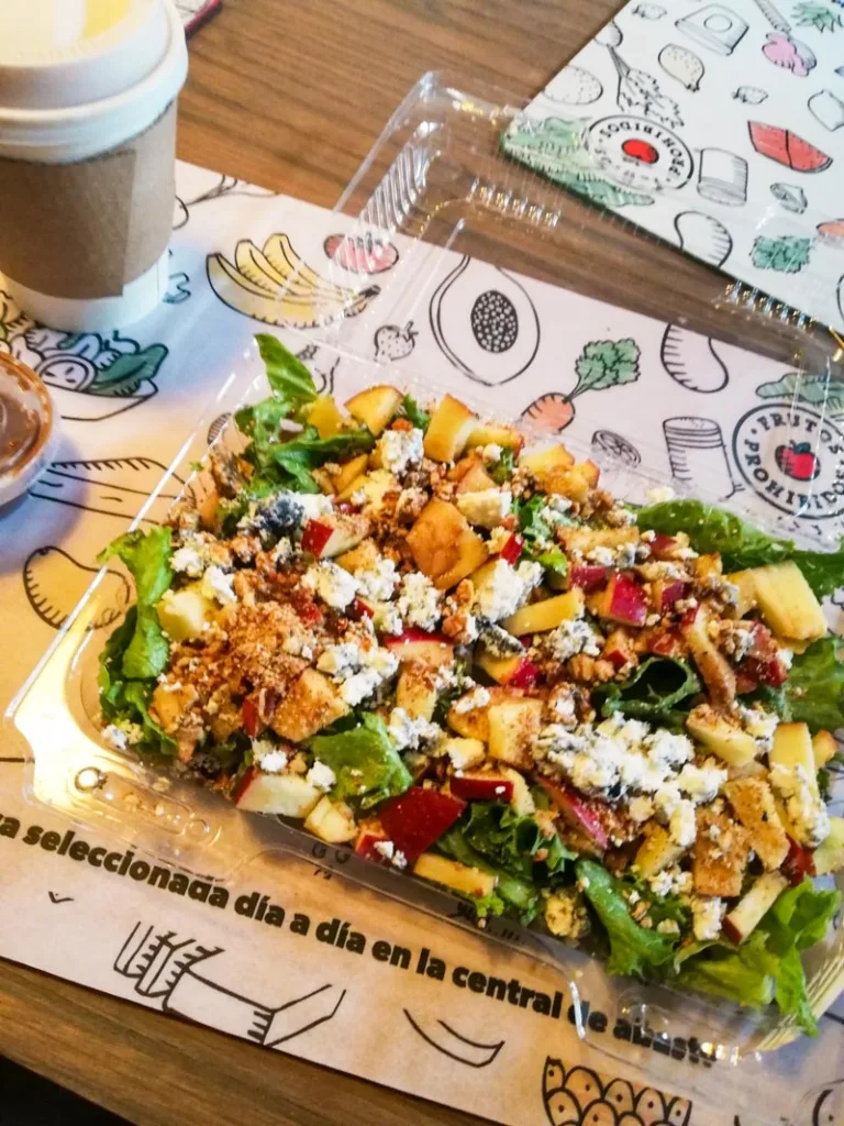A plastic container with a salad on a table at frutos prohibidos in roma norte, mexico city.