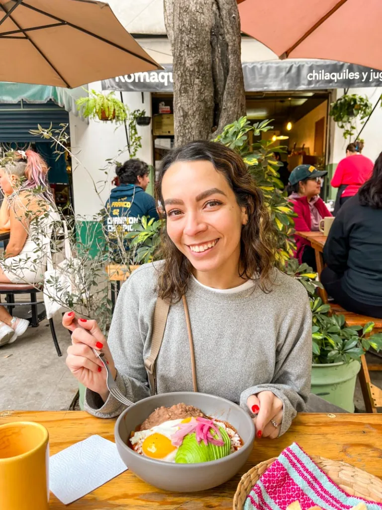 Smiling woman with a bowl of chilaquiles in front of her in Roma Norte, Mexico city