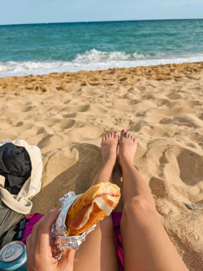 hand holding a jamon sandwich at the beach in barcelona