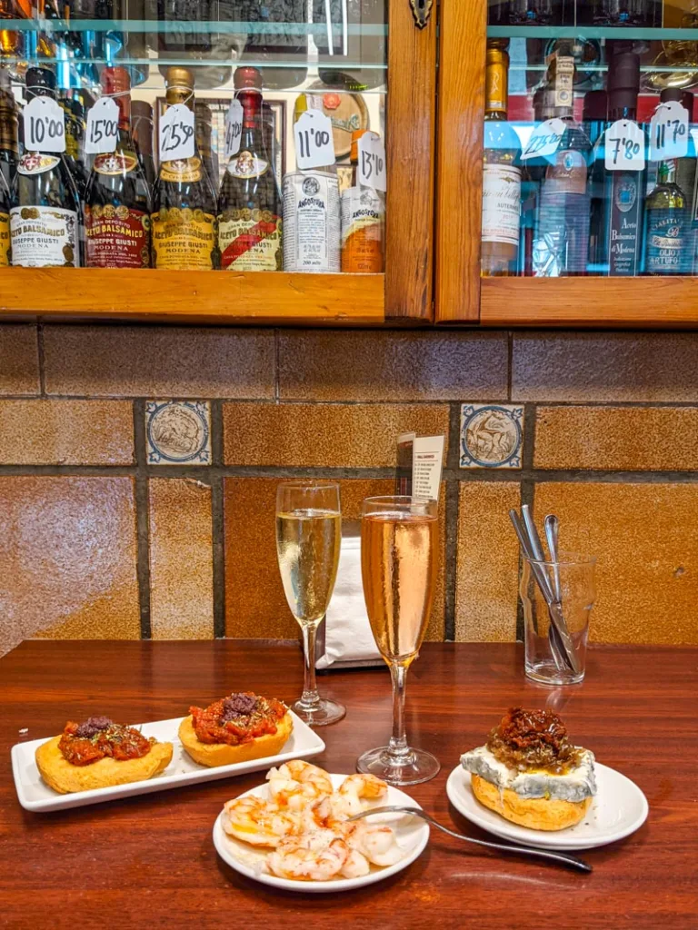 various tapas plates at quimet and quimet  in barcelona: a shrimp plate, a goat cheese tapa, two small sundried tomate tapas, and two glasses of cava 