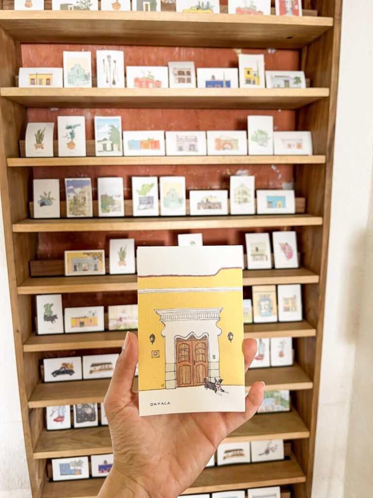 Hand holding a postcard of a colonial house in Oaxaca City inside an artists workshop