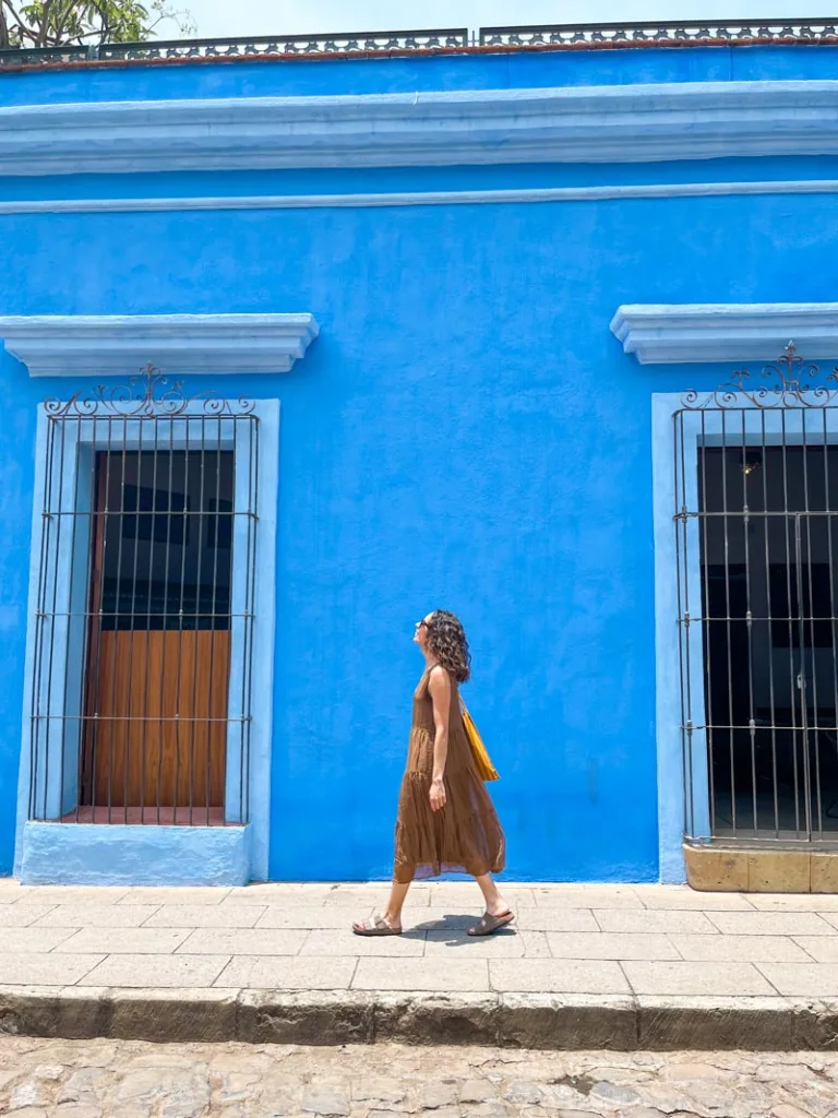 woman walking in front of a bright blue house in oaxaca city