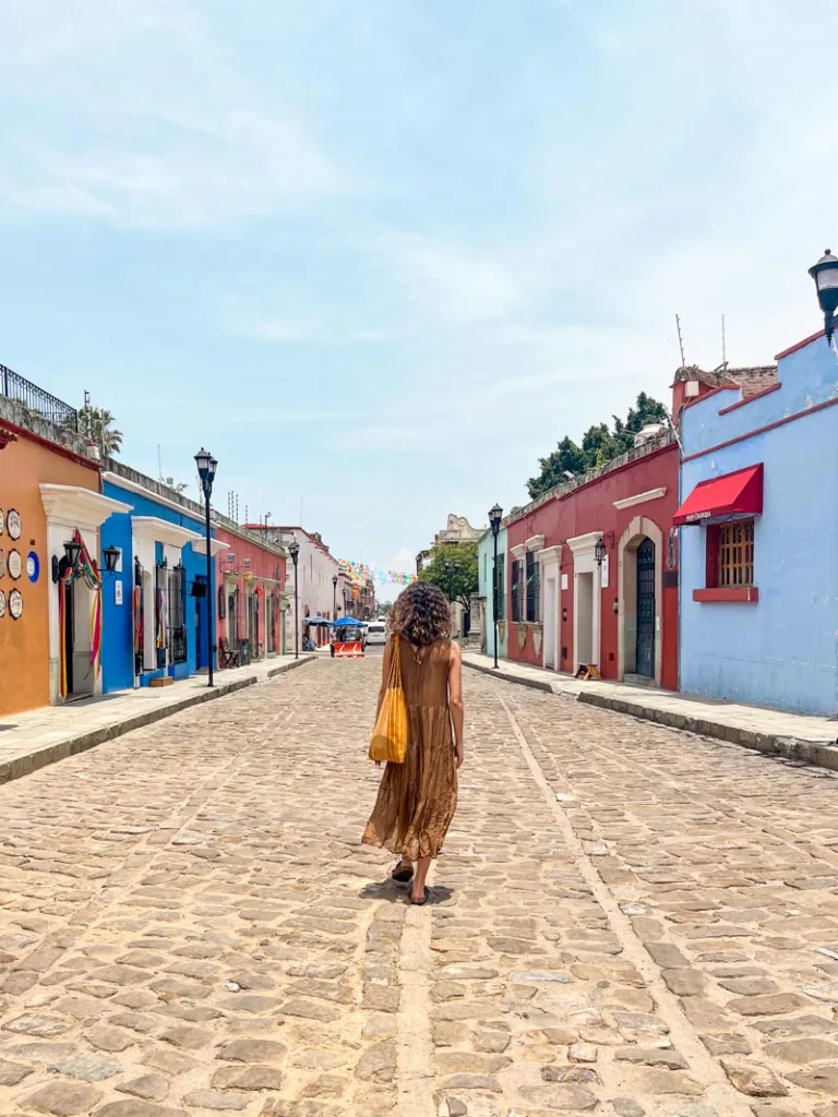 woman walking through a street lined with colorful colonial houses in oaxaca city
