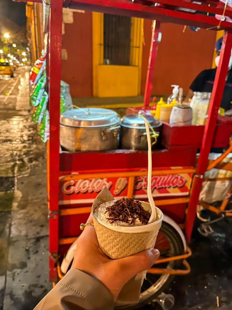hand holding a corn in a cup in front of the street food stand in oaxaca city