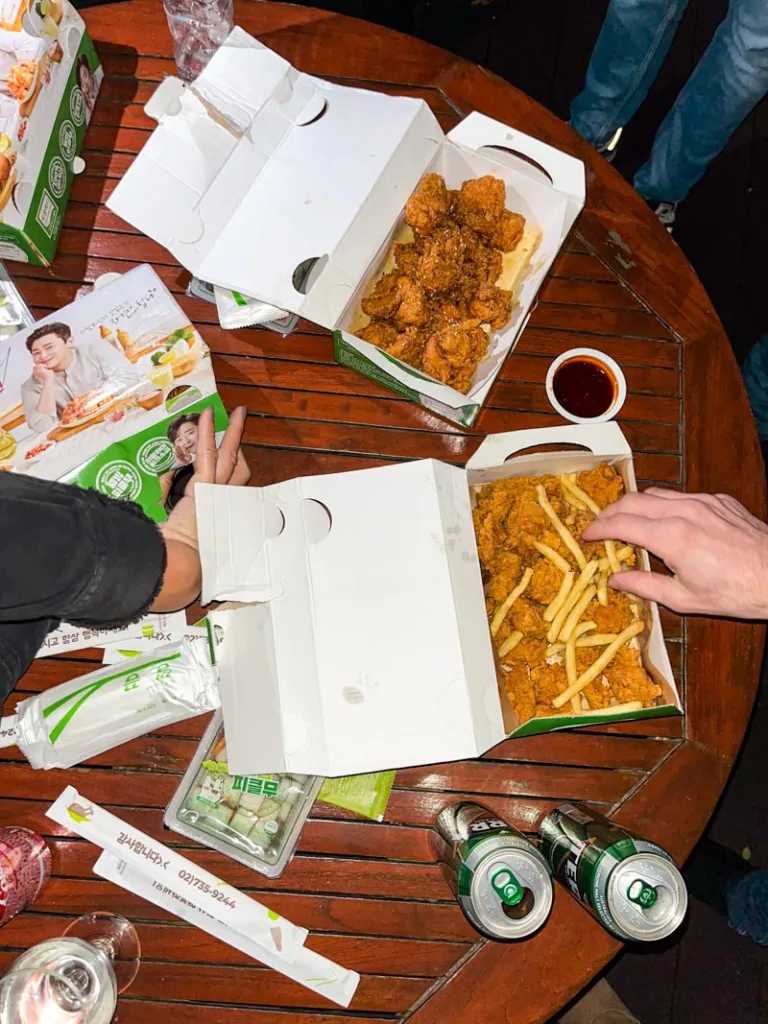 take-away boxes of korean fried chicken and fries on a wooden table