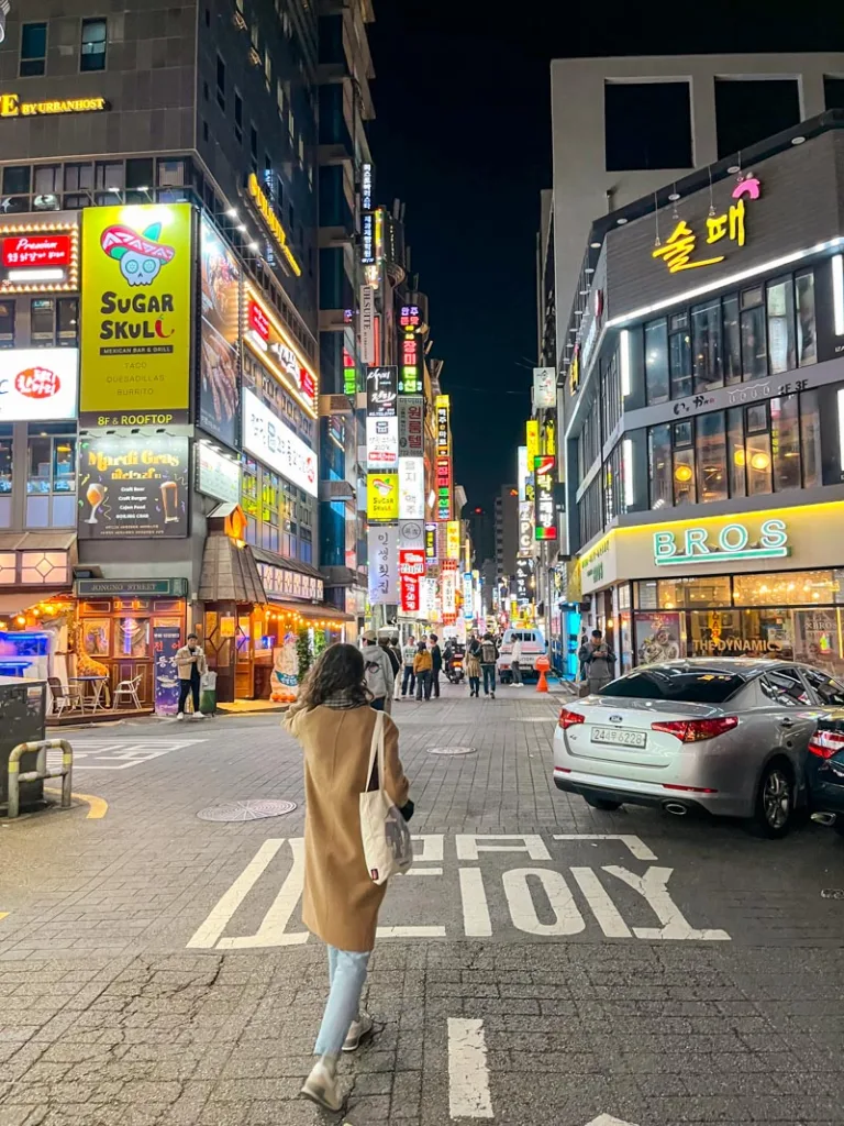 woman walking through a myeongdong street in seoul, lined with bright advertisements from bars and restaurants