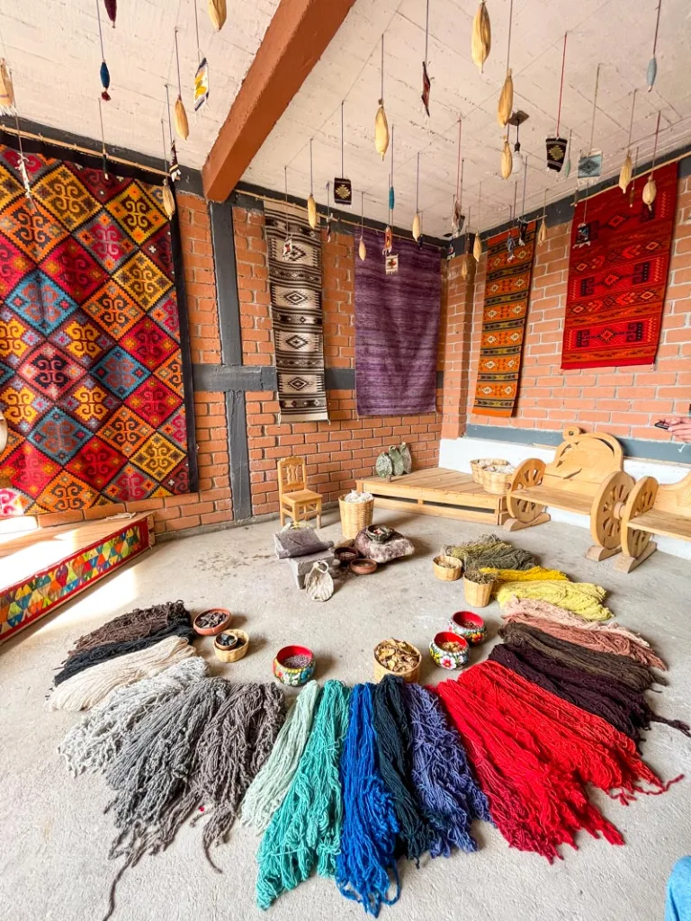 colorful wool yarn on the floor at a workshop with wool rugs hanging from the walls in oaxaca