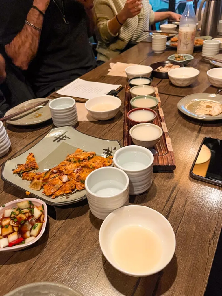 many small bowls of wine rice, and plates with korean pancakes on a table at a rice wine bar in seoul