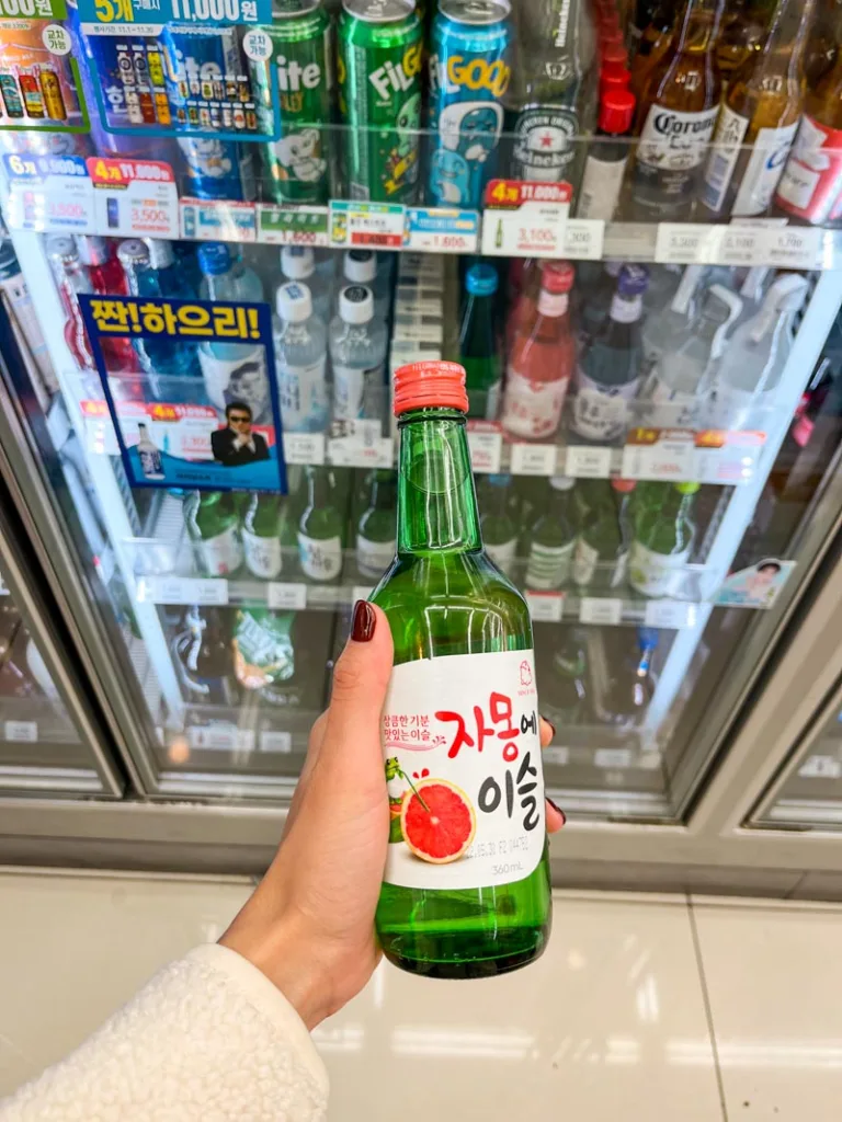 hand holding a bottle of grapefruit soju in front of the convenience store fridge in seoul
