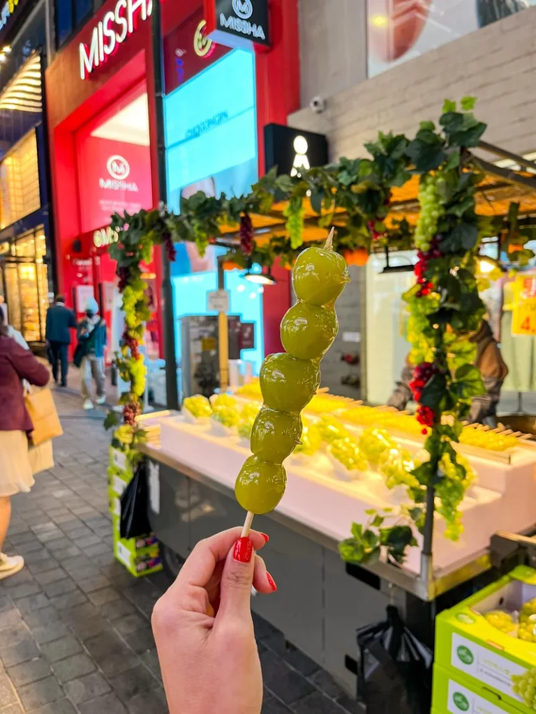 hand holding sugar-coated green korean grapes on a stick at myeongdong street food market in seoul
