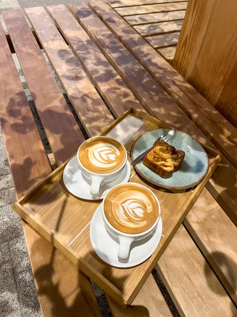 two lattes and a banana bread on a wooden tray on a wooden bench at blue bottle coffee in tokyo