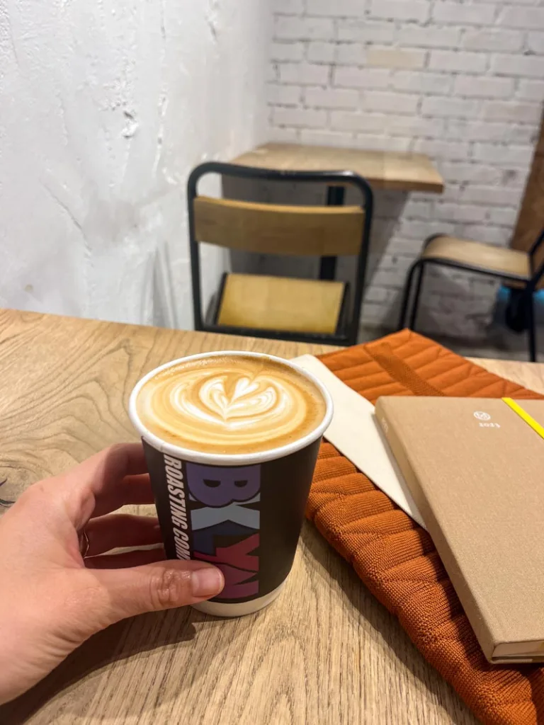 hand holding a to-go coffee cup on a wooden table at brooklyn roasteries in tokyo