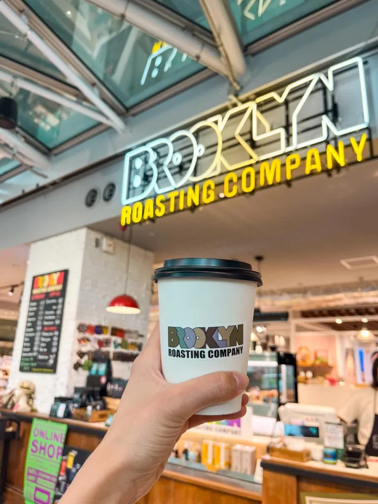 hand holding a to-go coffee cup at brooklyn coffee roastery in tokyo with a neon sign at the back