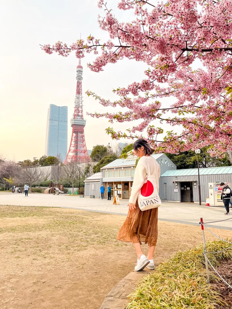 woman standing next to a cherry blossom tree with a view of the tokyo tower