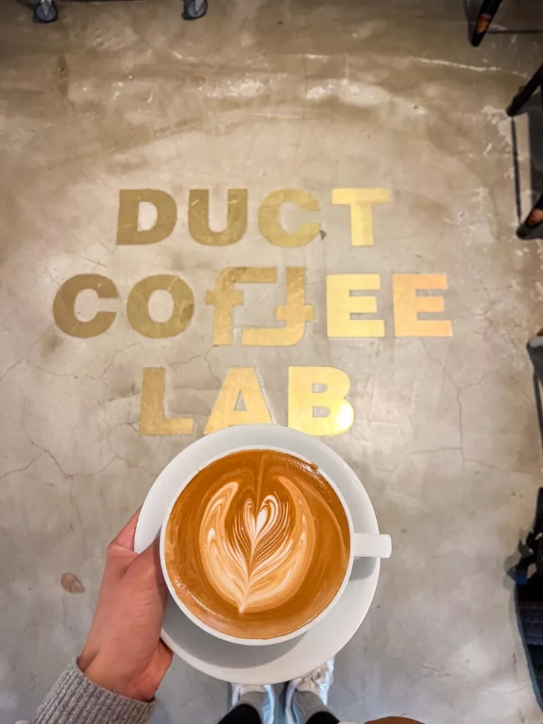 hand holding a latte with a view of the floor tile spelling out "duct coffee lab" in tokyo