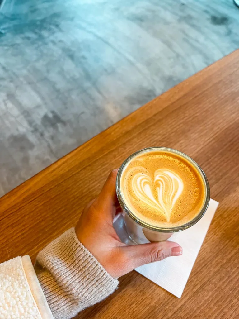 hand holding an hot latte on top of a wooden talbe at fuglen coffee shop in tokyo