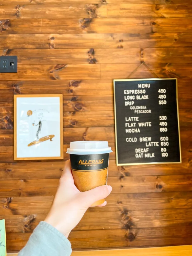 hand holding a to-go coffee cup in front of the menu at allpress espresso coffee shop in tokyo
