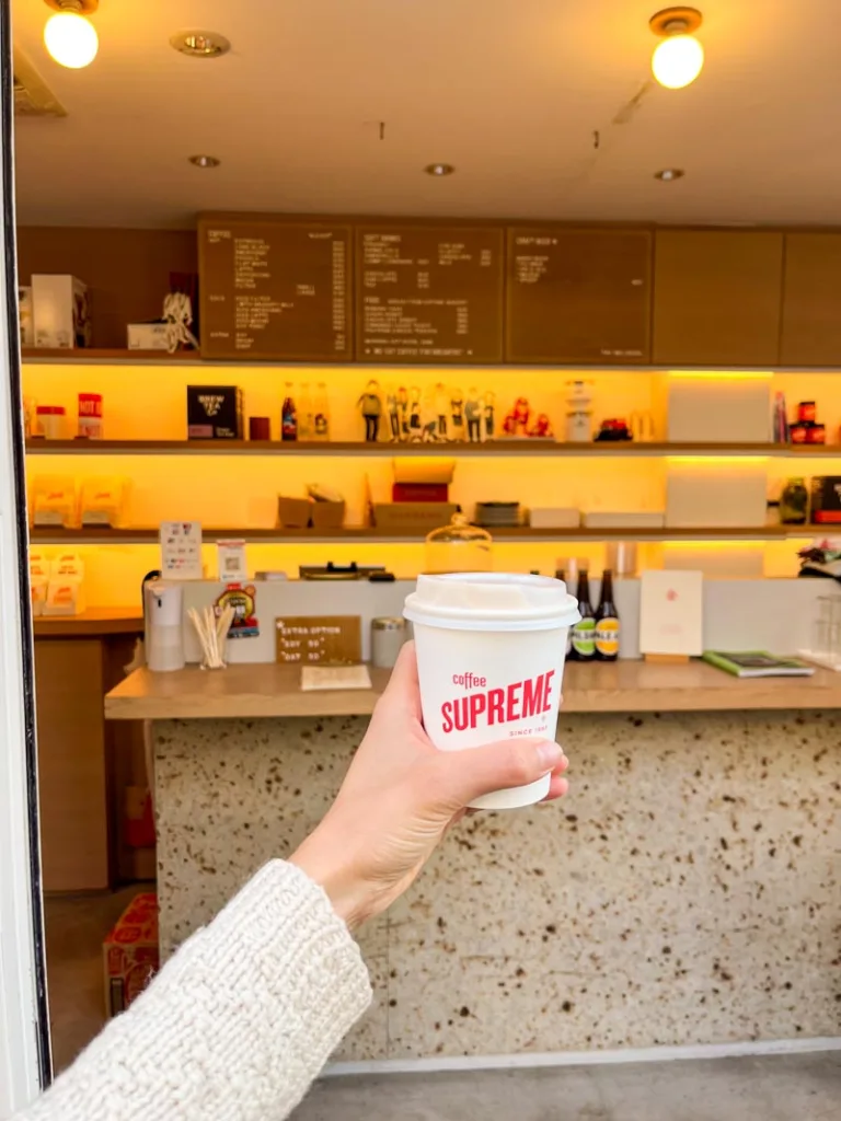 hand holding a to-go coffee cup with the view of the cream-colored bar at coffee supreme tokyo