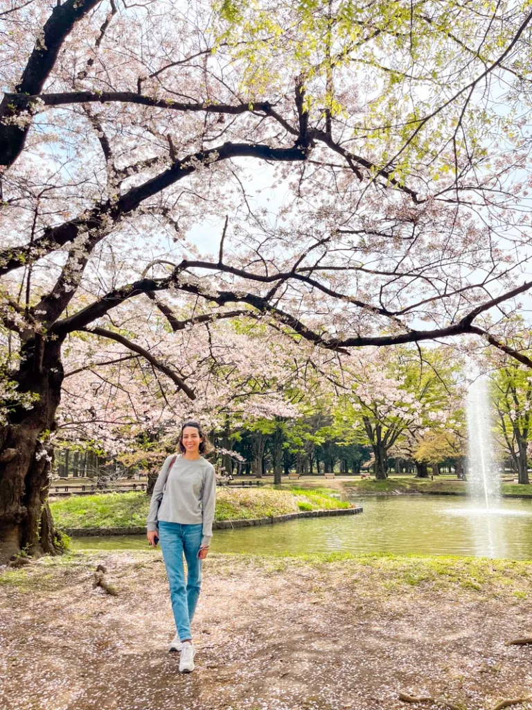 woman standing in front of an artificial lake surrounded by trees and a cherry blossom tree at Yoyogi Park in Tokyo