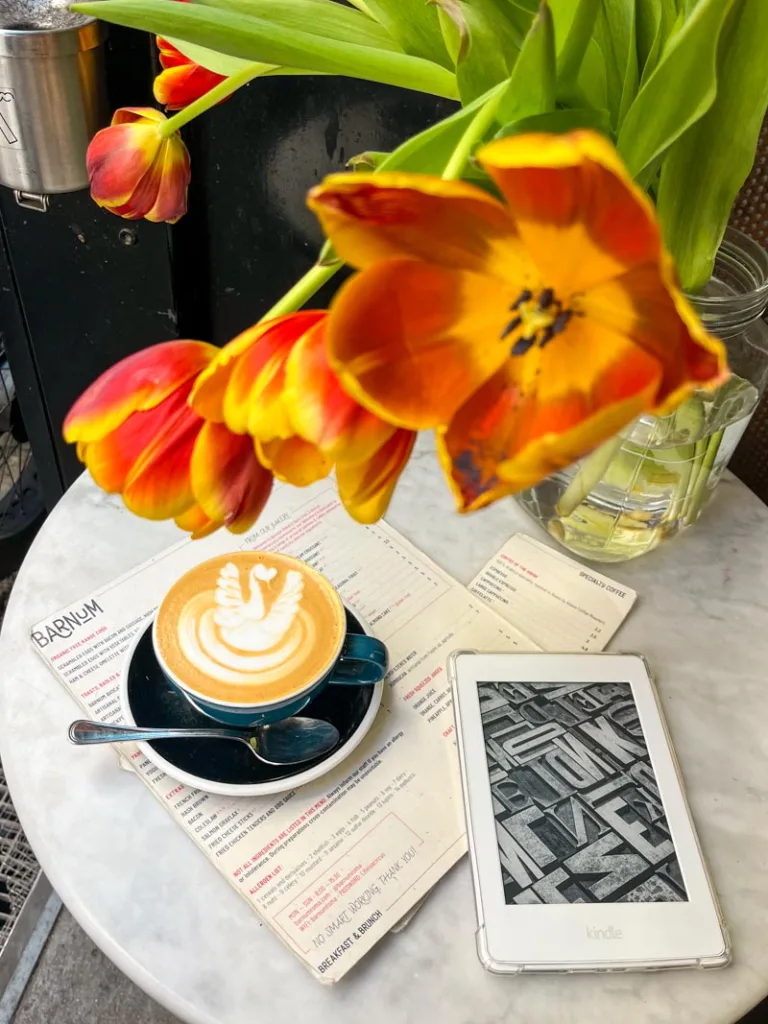 a latte on top of the menu, a kindle and red and yellow tulips on a table at barnum coffee shop in rome