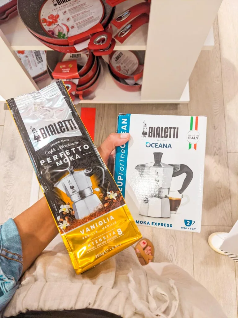 hand holding a moka pot in its box and a bag of ground coffee at a bialetti store in rome