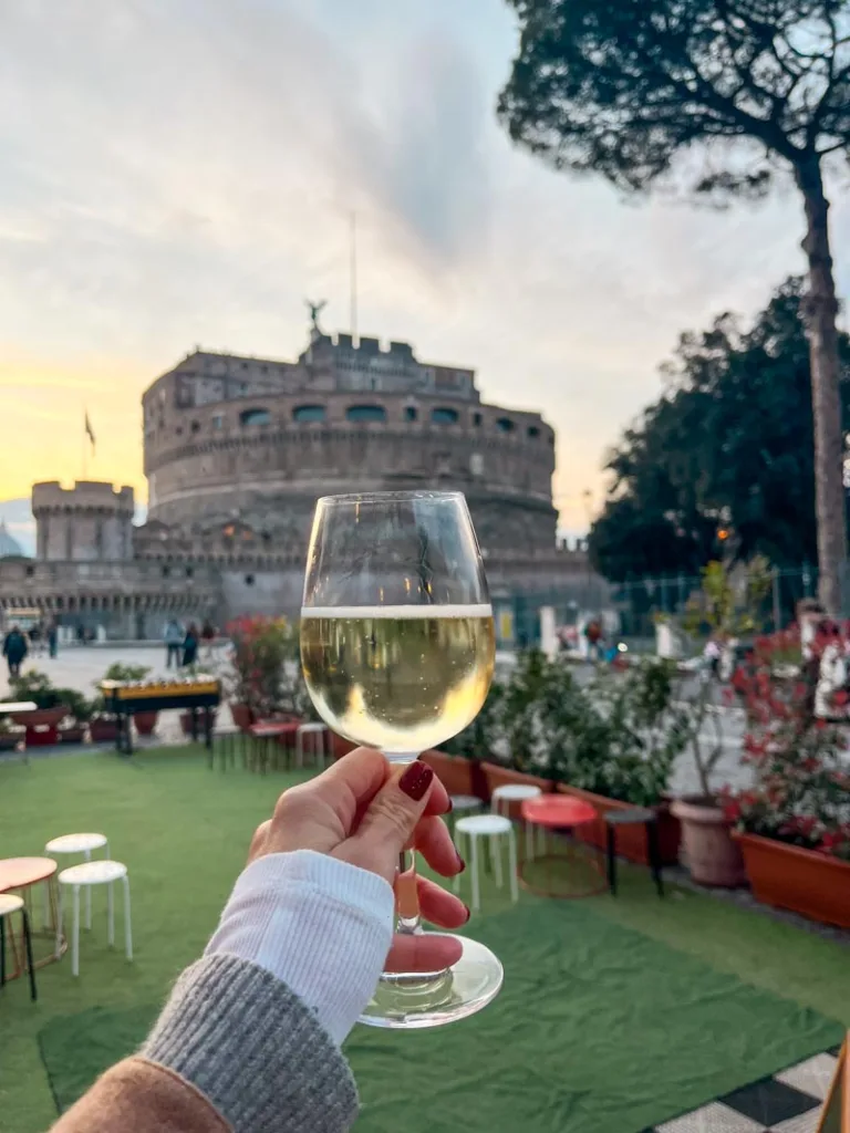 hand holding a glass of wine with a view of the castel sant'angelo behindg