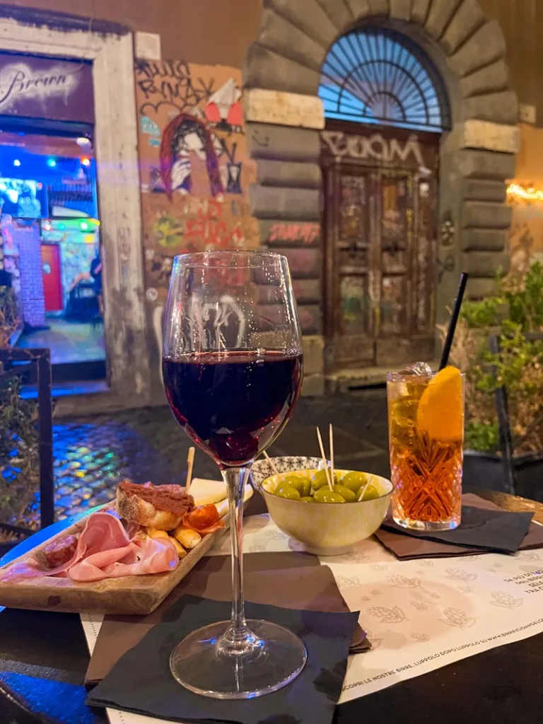 a meat and cheese board, a glass of red wine and a spritz on an oudoor table in trastevere rome