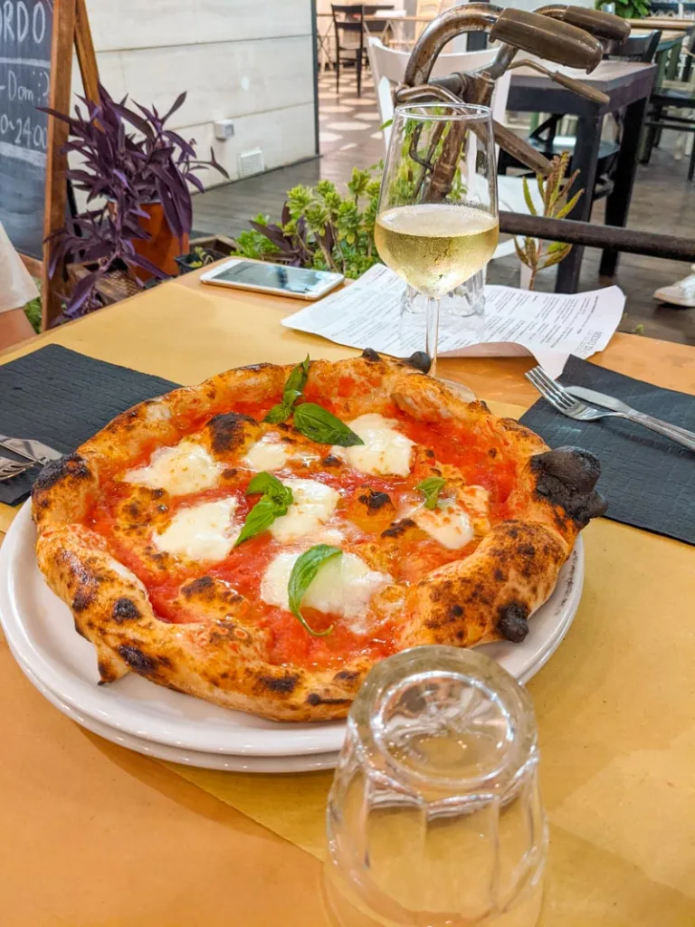 a margherita pizza in the center of a table and a glass of white wine at bordo pizzeria in pigneto