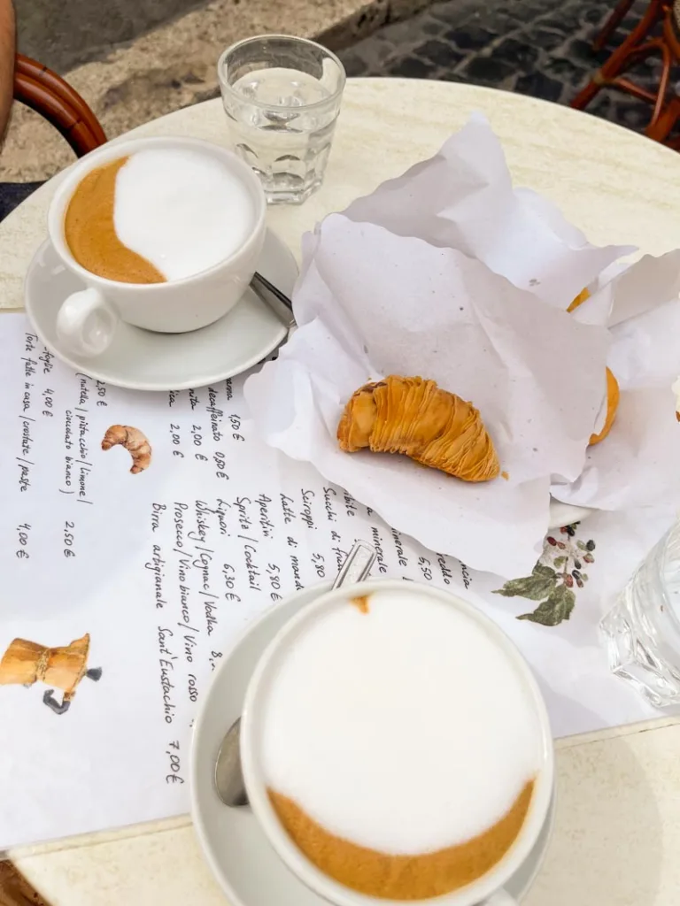 two gran cappuccinos and small pastries on an outdoor table at caffe sant eustachio in rome