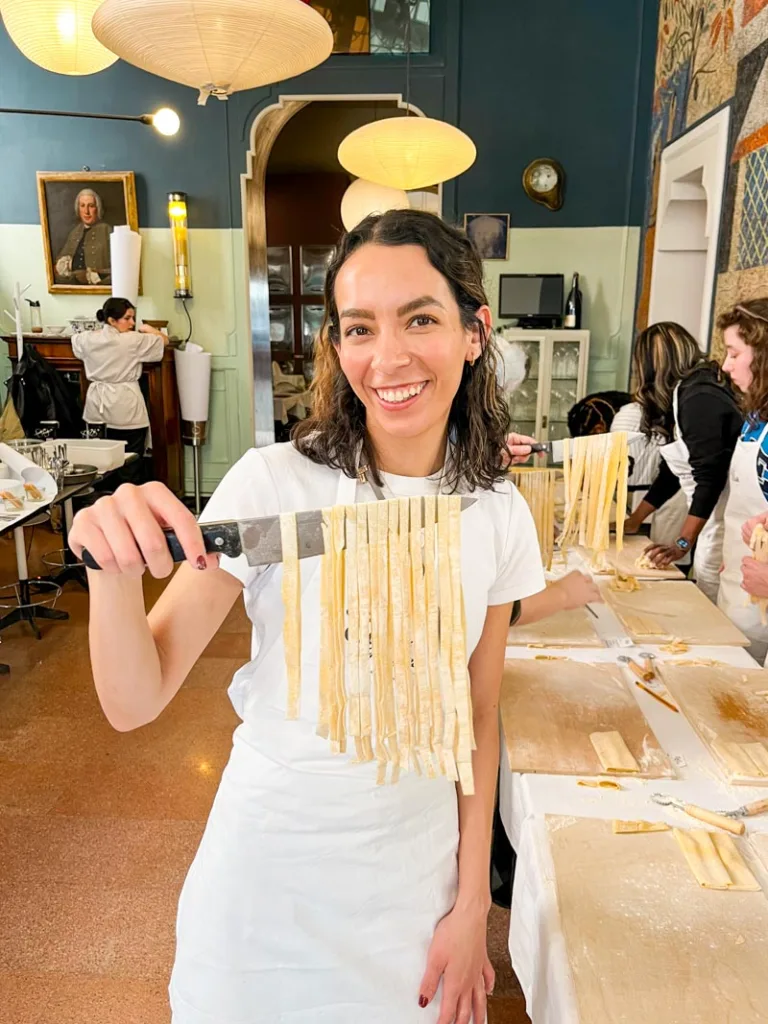 woman holding a knife with homemade fettuccine pasta hanging from it at a cooking class, one of the best unique things to do in rome