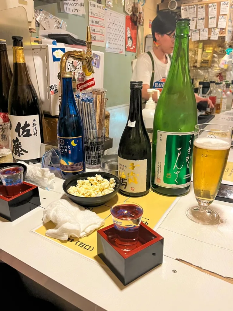 a small bowl of popcorn, sake bowls, and sake bottles at a snug bar in golden gai in shinjuku, tokyo