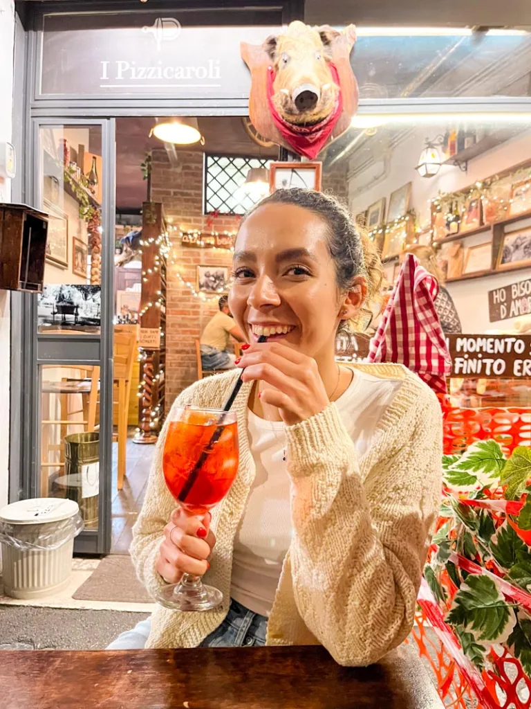 woman sipping on an aperol spritz at an outdoor table at i pizzicaroli in rome