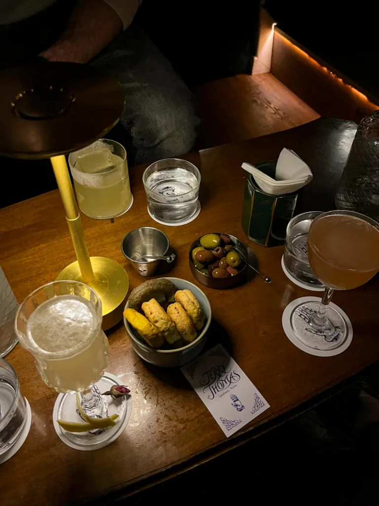 dimly lit low wooden table with cocktails, taralli, and a small olive plate at Jerry Thomas Speakeasy in rome