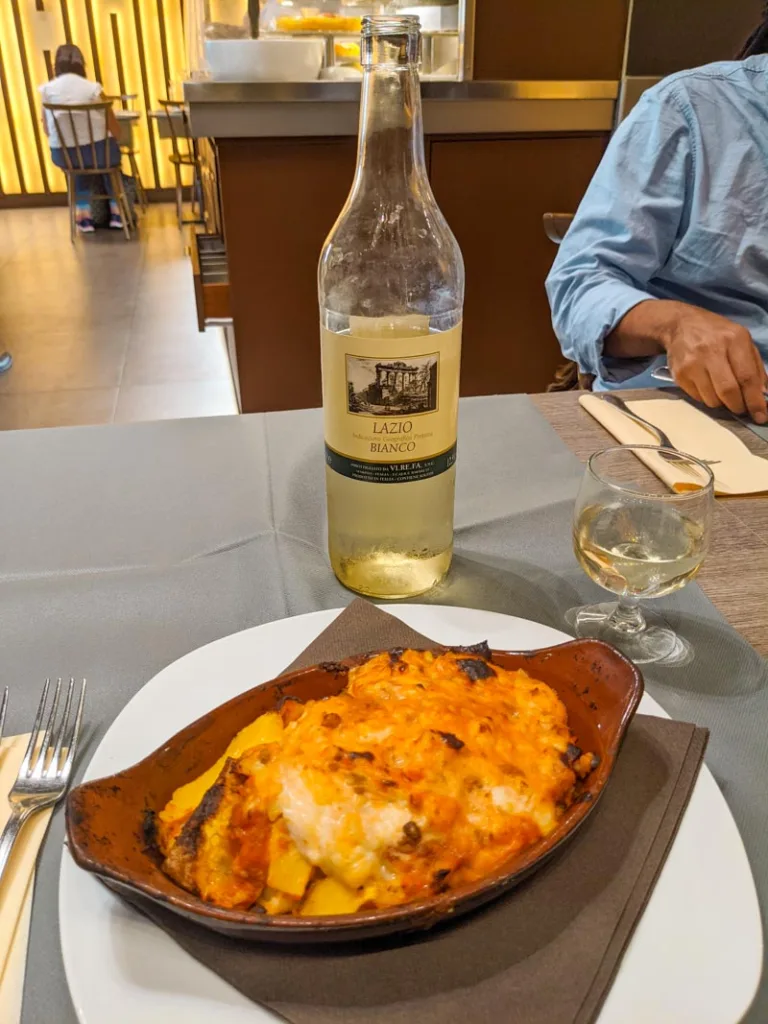 a plate of lasagna and a bottle of white wine at la famiglia, a local roman restaurant