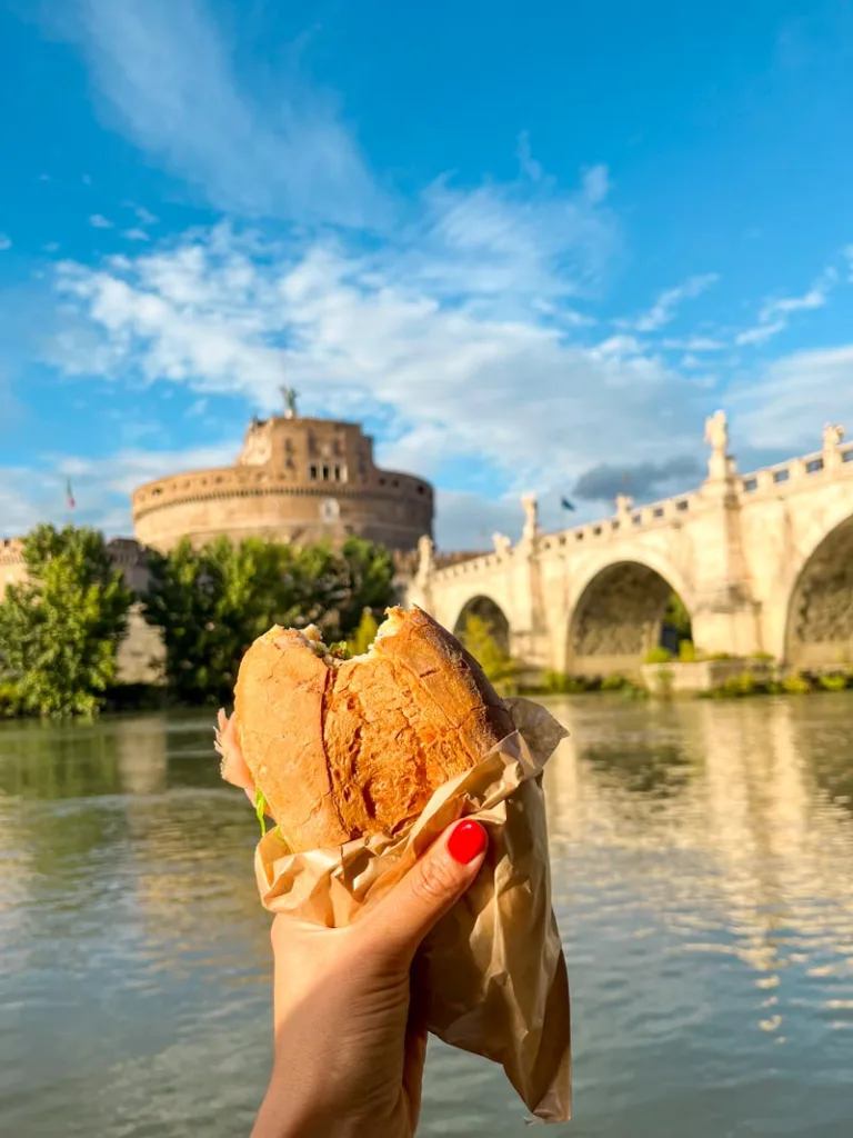 hand holding a panino overlooking the river tiber in rome