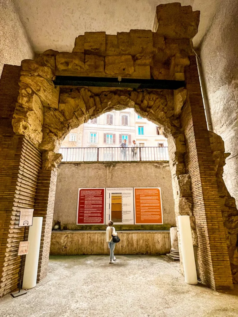 woman on an underground level looking up at the arch that use to be the entrance to the palace of domitian under piazza navona in rome