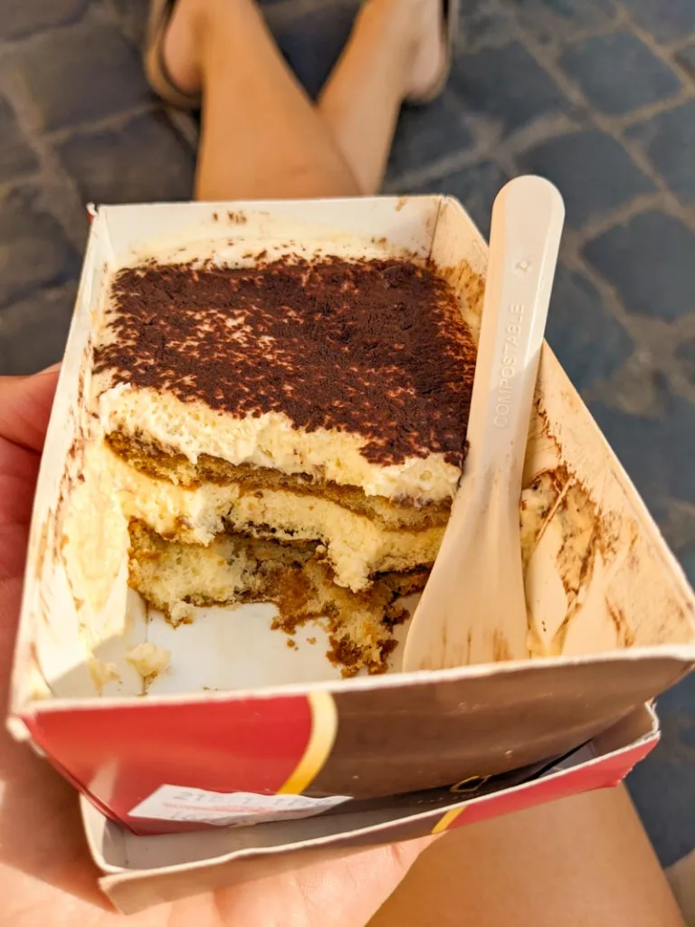 hand holding a half-eaten box of tiramisu from pompi in rome