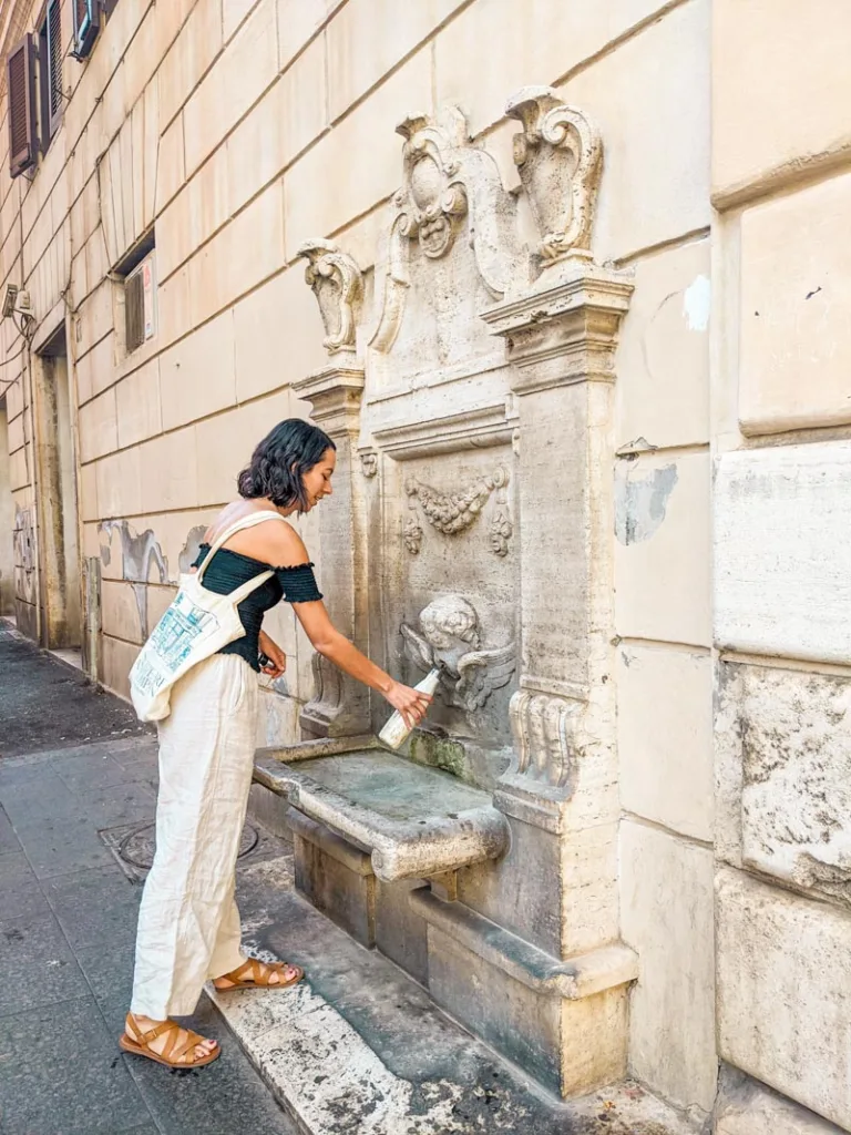 woman filling up a water bottle at a public water fountain in rome