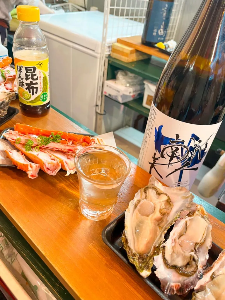 crab legs, two massive oysters, and a sake cup next to a sake bottle at a standing sushi bar in ameyoko shopping street