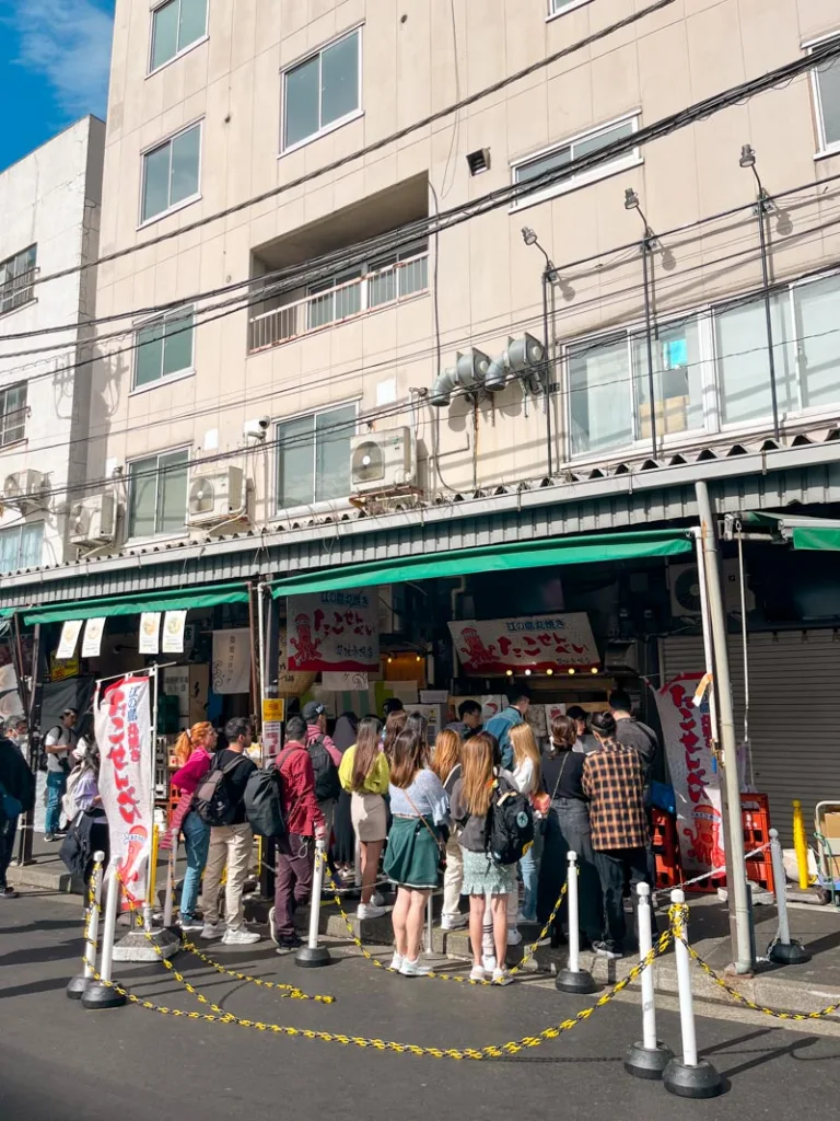 people standing in line outside a food stand at the tsukiji fish market in tokyo