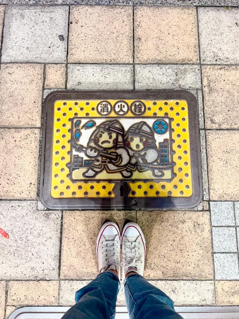 cute yellow manhole in tokyo showing two cartoon samurai holding a hose