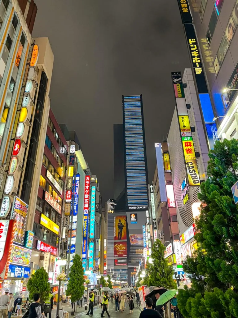 neon sign covered skyscrapers in shinjuku, tokyo with a view of a godzilla statue peeking through the buildings