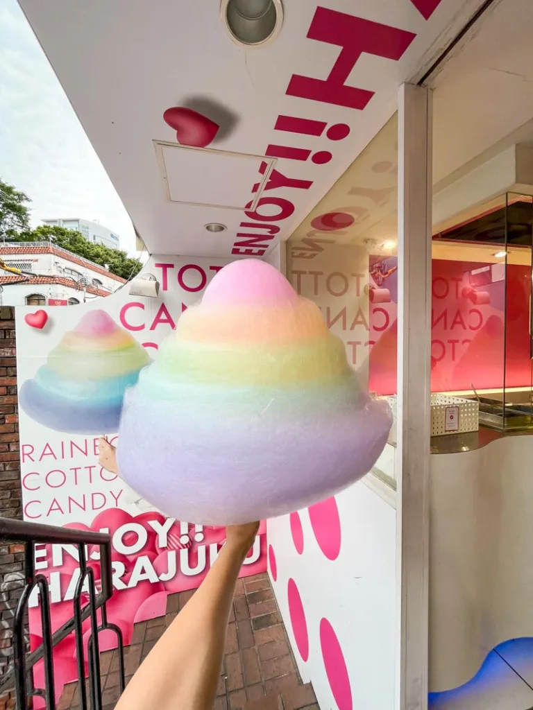 hand holding a massive, rainbow-colored cotton candy in harajuku, tokyo