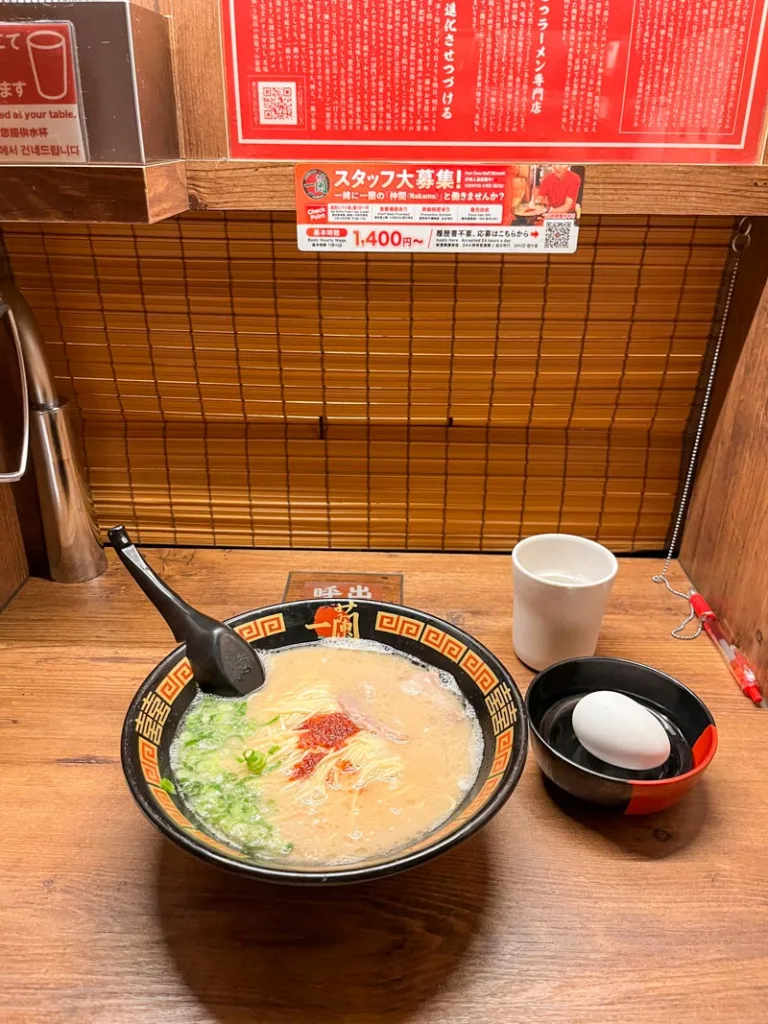 a bowl of ramen, with a side of hard boiled egg and a glass of water at an individual booth at ichiran ramen in tokyo
