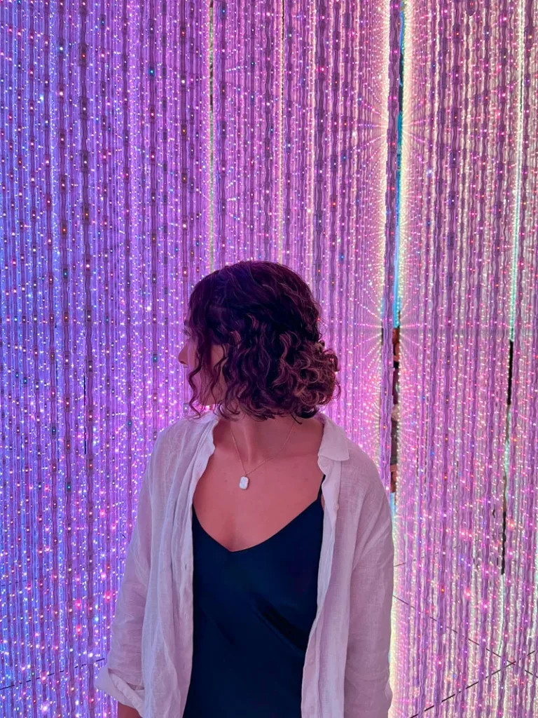 woman standing in front of multiple lilac and purle led string lights at team lab planets tokyo