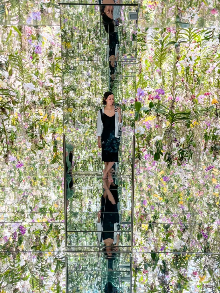 woman standing in front of a mirror, on mirror floor, reflection endless flowers at teamlab planets