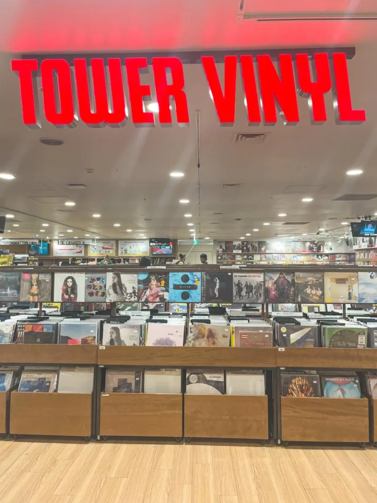 red neon lights "tower vinyl" sign on top of boxes with vinyl records at tower records in tokyo