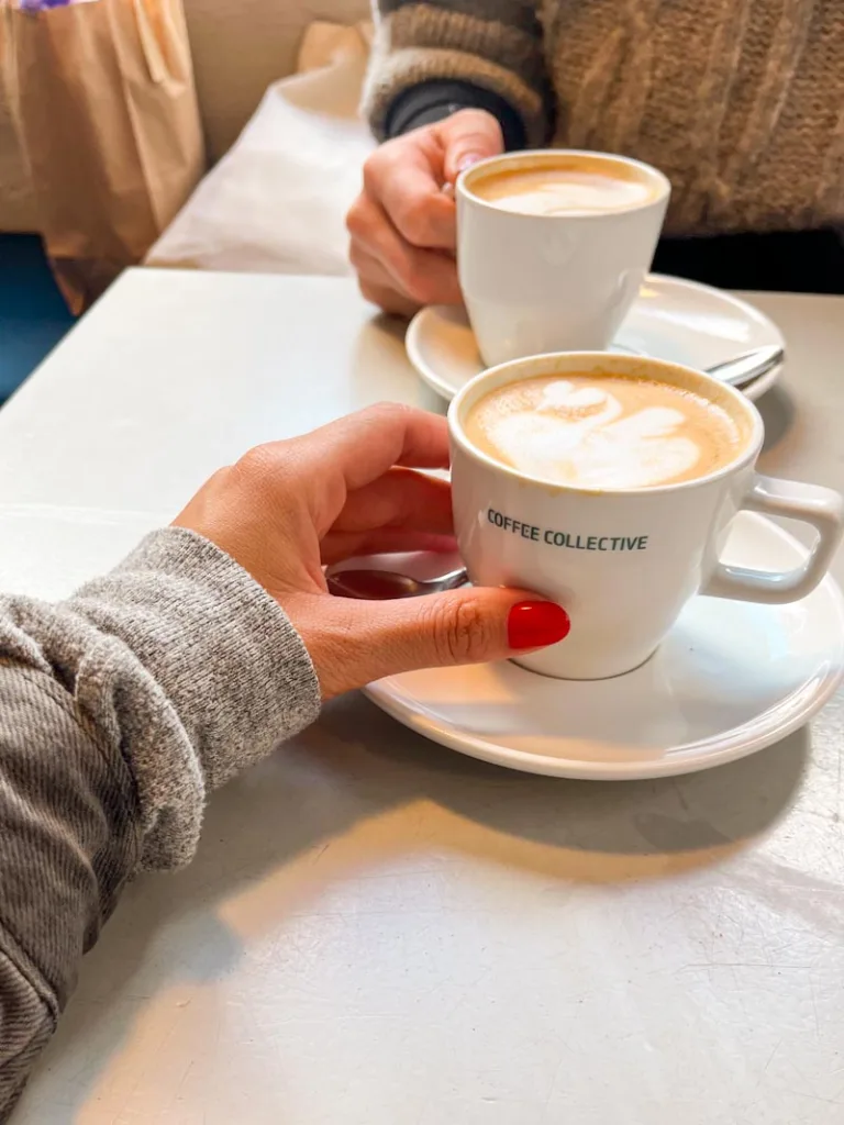 two hands holding a cappuccino cup each, on a table at coffee collective in copenhagen