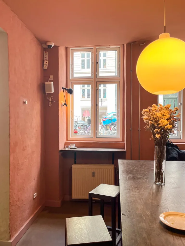 dark pink walls, a long wooden table with stools at coffee collective in copenhagen